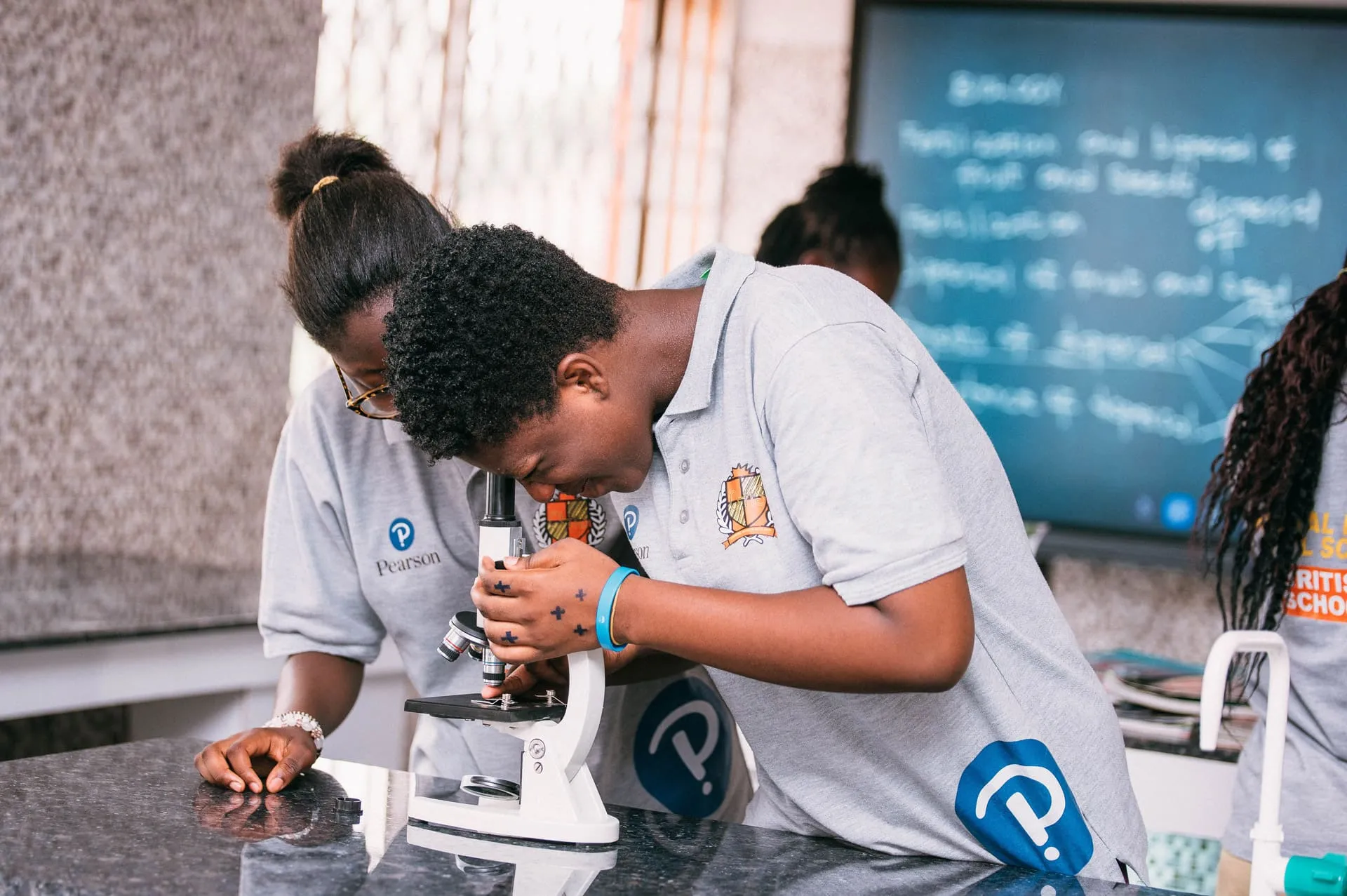 Crystal Heights students working with a microscope in the science laboratory, in Pearson-branded shirts